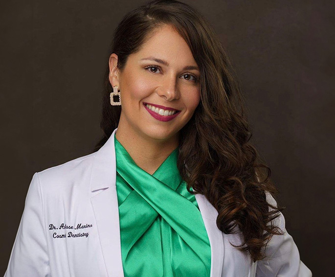 The image features a woman wearing a white lab coat with green accents, standing against a dark background.