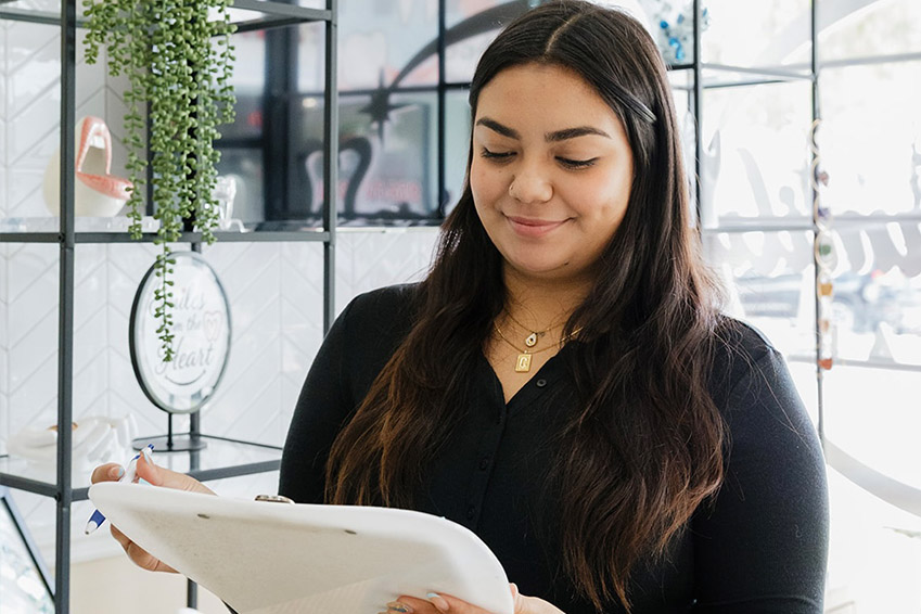 In the image, a man is making a heart shape with his hands while smiling at the camera. He appears to be in a dental or medical setting, as suggested by the presence of medical equipment and personnel in the background.