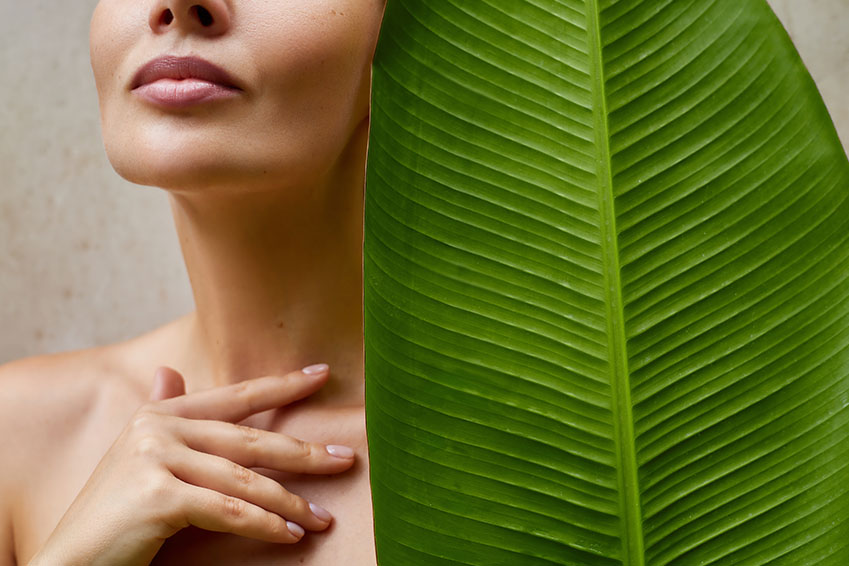 A person s face behind a large green leaf with a visible vein pattern.