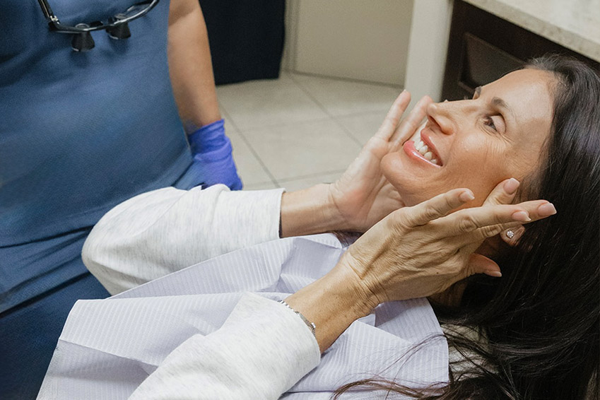 A young woman with a joyful expression holds up a large green palm leaf to her face.