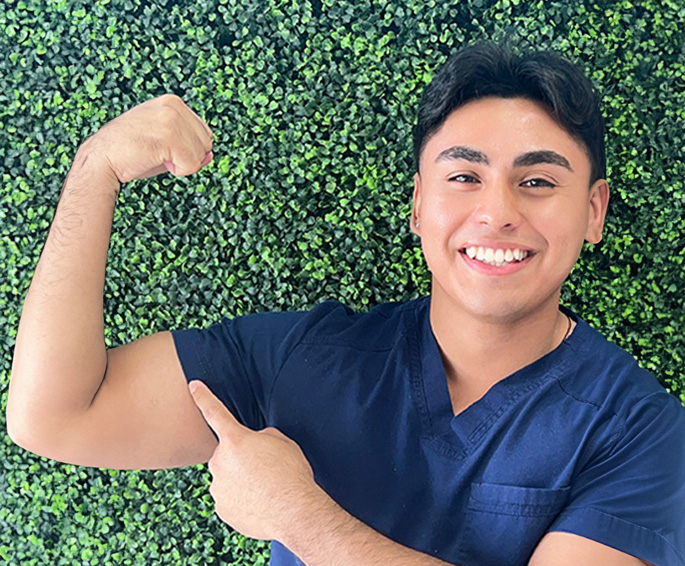 A man in a blue shirt flexing his bicep while smiling at the camera.