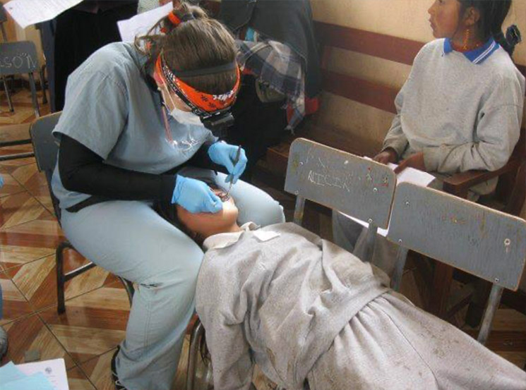 A dental hygienist providing care at a makeshift dental clinic with a patient seated on a chair.