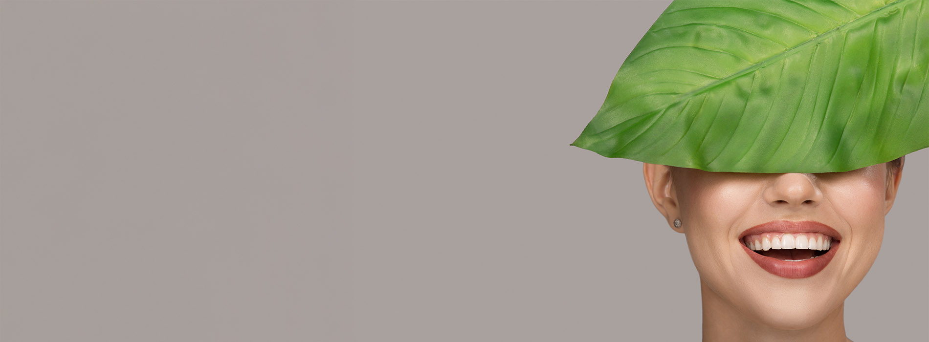 The image shows a person with a large green leaf covering their head, smiling at the camera.