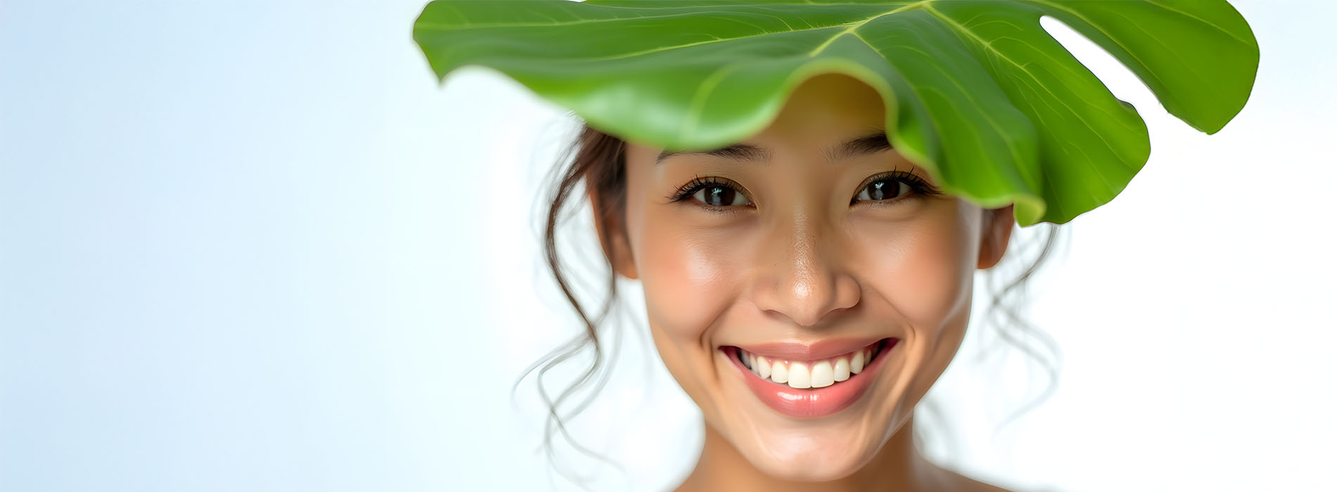 A woman with a broad smile peeking out from behind a leafy green plant.