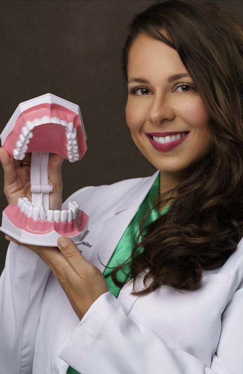 A woman wearing a white lab coat holds up a large model of a human mouth with open teeth.