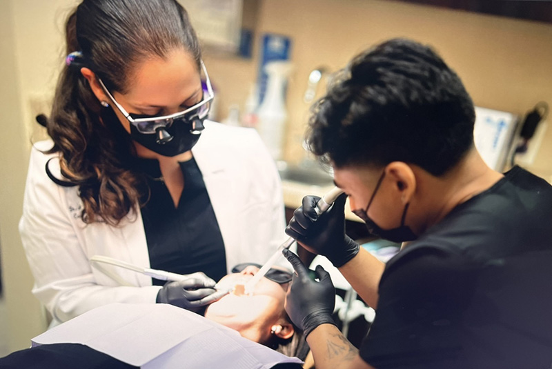 A dentist and dental hygienist performing oral care procedures on a patient in a dental office setting.