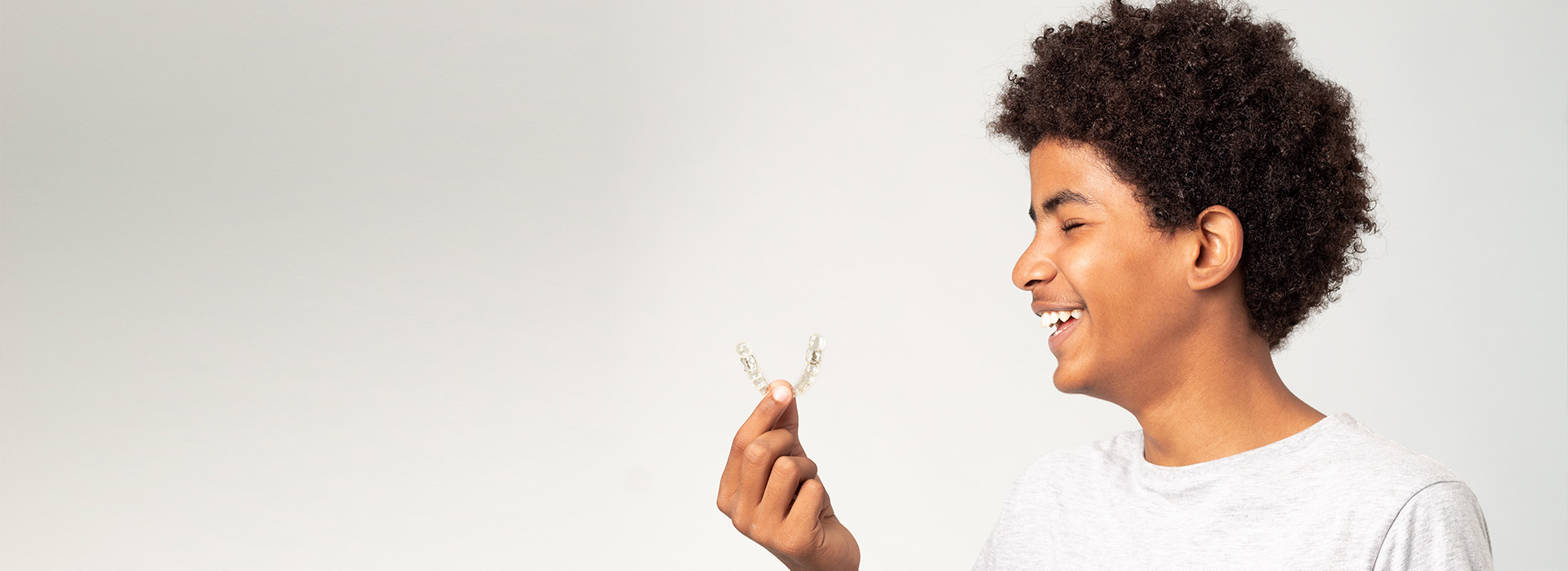 A young person with curly hair looking upwards while holding a small object between their fingers.