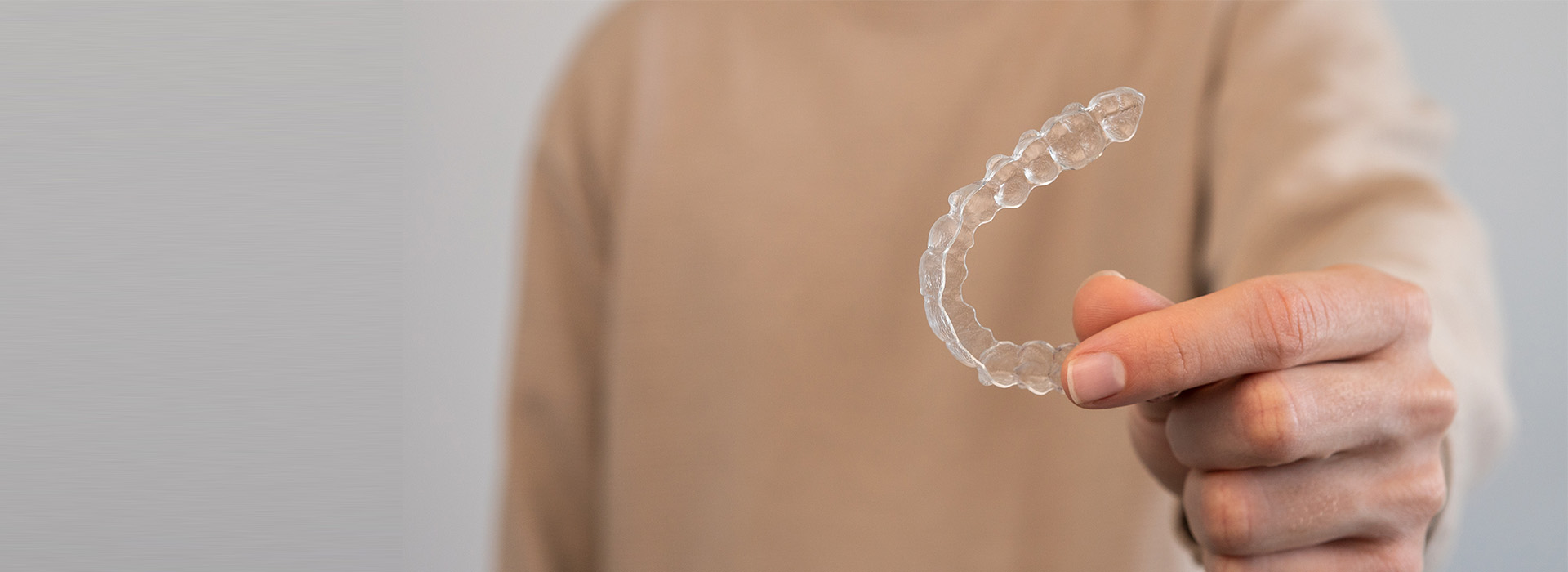 The image shows a person s hand holding an object that resembles a clear plastic ring with a fingerprint-like pattern on it, against a blurred background.