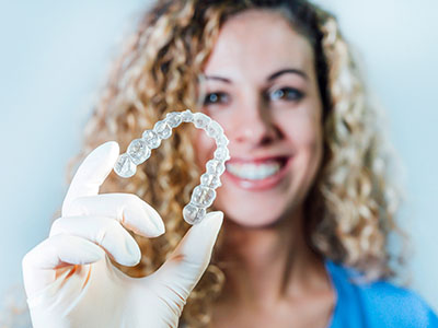 A woman holding up a clear plastic dental retainer.
