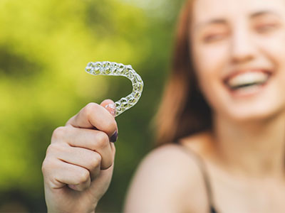 A smiling woman holds up a large toothbrush with bristles, suggesting dental hygiene.